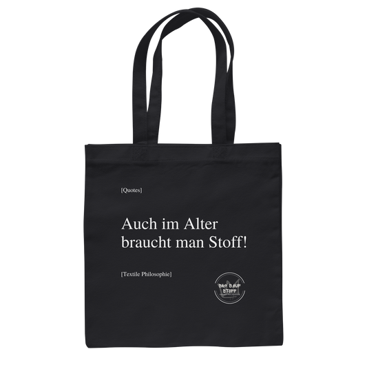 Schwarzer Jutebeutel mit weißer Aufschrift "Auch im Alter braucht man Stoff" und Logo "Sag´s auf Stoff"