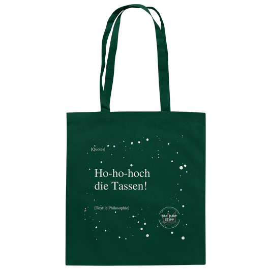 Grüner Jutebeutel von „Sag’s auf Stoff“ mit weißer Aufschrift "Ho-ho-hoch die Tassen!", Weißen Schneeflocken im Hintergrund und Logo "Sag´s auf Stoff". Perfekt als Geschenk.