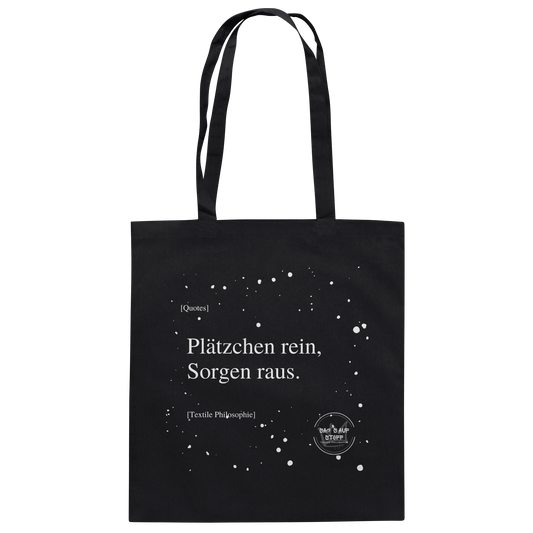 Schwarzer Jutebeutel von „Sag’s auf Stoff“ mit weißer Aufschrift "Plätzchen rein, Sorgen raus.", Weißen Schneeflocken im Hintergrund und Logo "Sag´s auf Stoff". Perfekt als Geschenk.